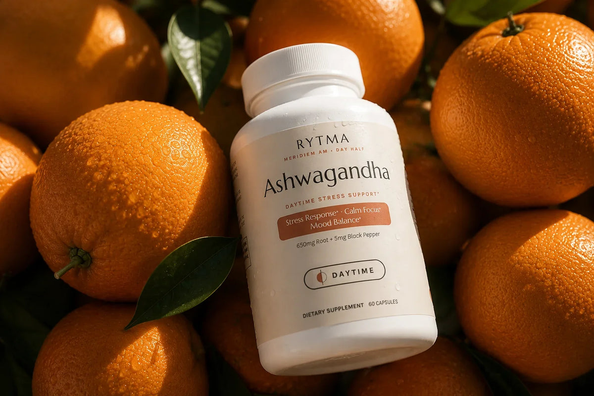 Rytma Ashwagandha bottle resting among fresh whole oranges and glossy green leaves in warm sunlight.